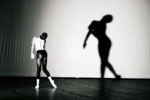 A graceful ballet dancer in a leotard with a captivating shadow on stage.